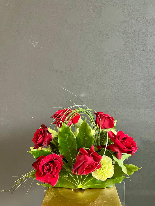 Composizione con rose rosse, garofani, bear grass e foglie di aralia